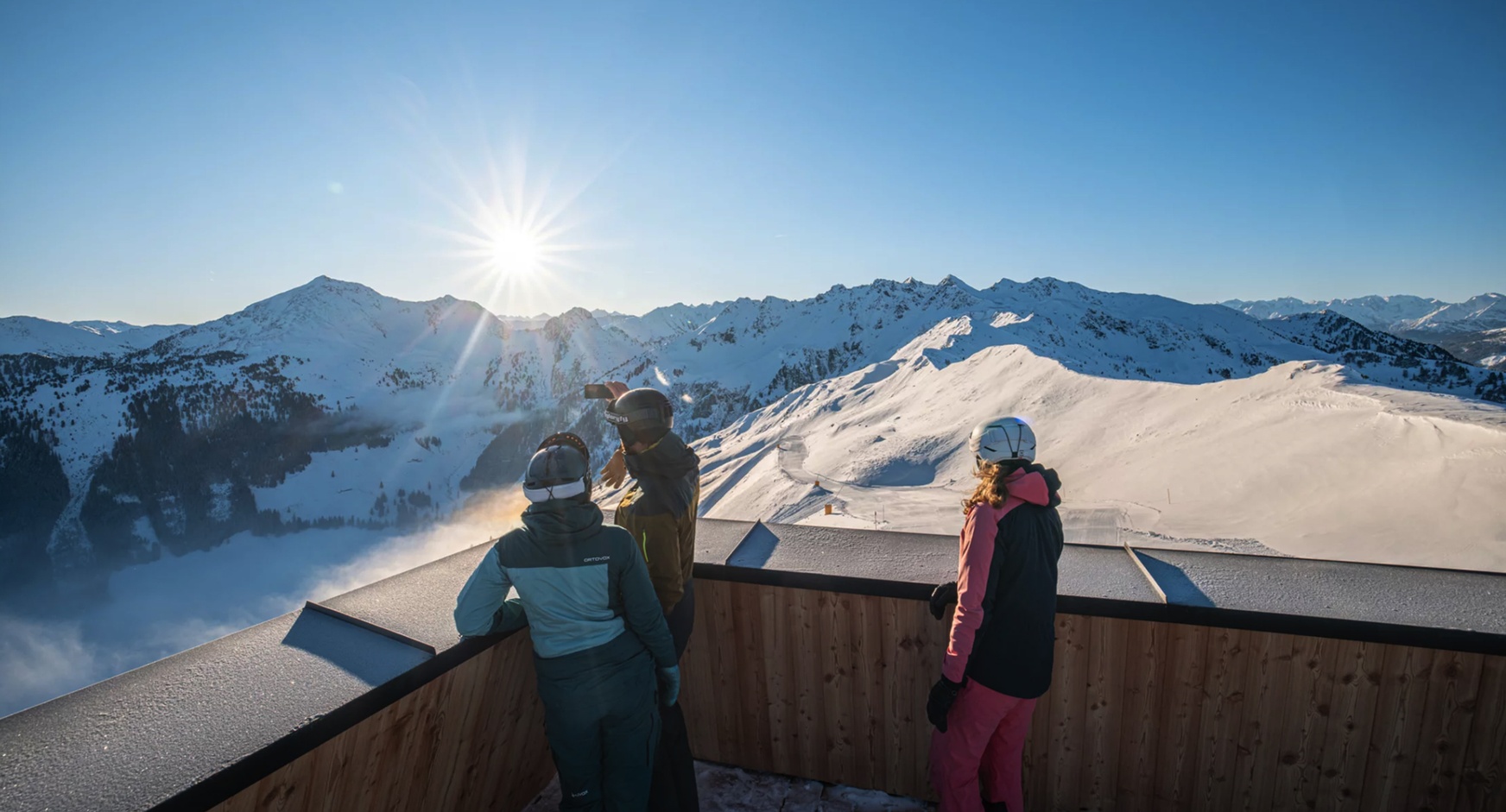 Drei Personen betrachten auf einer Terrasse stehend die Berge