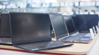 Viele aufgeklappte Laptops stehen auf einem Tisch. Die Bildschirme sind schwarz. Vor manchen steht ein Schild