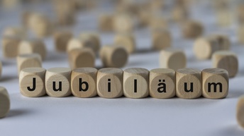 Jubiläum, Holzwürfel mit Buchstaben im Vordergrund, in der Unschärfe verschwommen noch weitere Würfel ohne Buchstaben