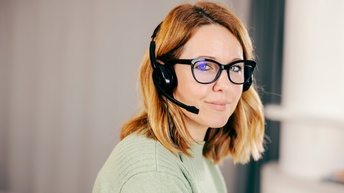 Portrait einer rothaarigen Person mit schwarzen Brillen und Headset, Hintergrund verschwommen