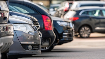 Motorhaube eines parkenden Autos im Fokus, daneben weitere parkende Autos in der Unschärfe