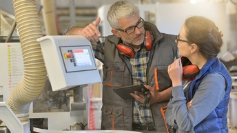 Personen unterhalten sich in einer Tischlerwerkstatt mit einem Tablet und einer Maschine