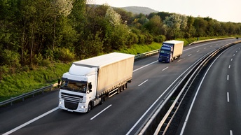 Zwei Lkws auf Autobahn fahrend umgeben von grünen Sträuchern