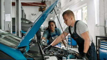 Zwei Personen in Autowerkstatt beugen sich über Motor eines Autos