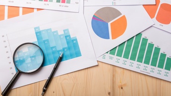 Mehrere Blätter mit Diagrammen, Lupe und Stift daraufliegend