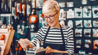 Person mit Brille, kurzen Haaren und gestreiftem Pullover steht bei einem digitalen EC-Karten Terminal in einem Shop