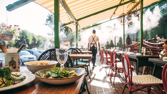 Gastgarten mit Markise und gedecktem Tischen, im Hintergrund Rückenansicht einer Person, die kellnert