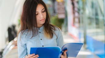 Junge Frau liest stehend in einer blauen Mappe