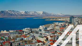 Stadtansicht von Reykjavik mit vielen roten Dächern mit modernen Hochhäusern; im Hintergrund sieht man das Meer und verschneite Berge