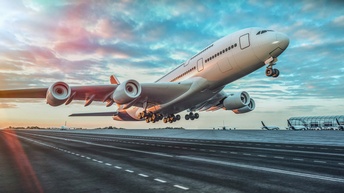 Großes Flugzeug beim Starten auf Landebahn im Licht des Sonnenuntergangs, im Hintergrund weitere Flugzeuge parkend