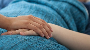 Die Hand einer Person liegt auf der Hand einer anderen Person, die mit einer blauen Decke zugedeckt liegt