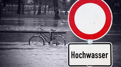 Fahrrad steht im Hochwasser; davor Warntafel