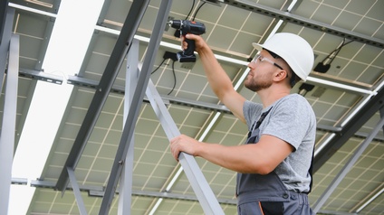 Person mit Schutzbekleidung verschraubt Metallgestell für Solaranlagen mit Akkuschrauber