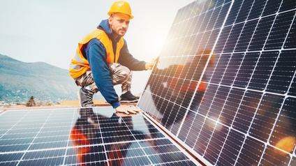 Person in Arbeitskleidung mit Schutzhelm und Warnweste montiert Solarpanele. 