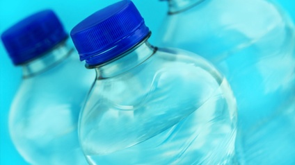 Nahaufnahme von drei Plastikflaschen mit blauen Verschlüssen, die mit einer durchsichtigen Flüssigkeit befüllt sind vor blauem Hintergrund