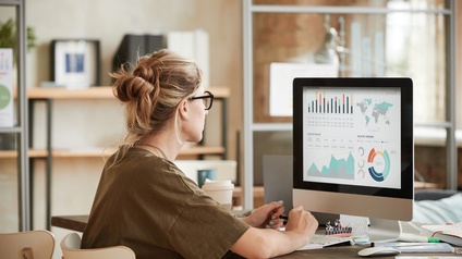 Person mit Brillen sitzt vor Computermonitor mit Diagrammen