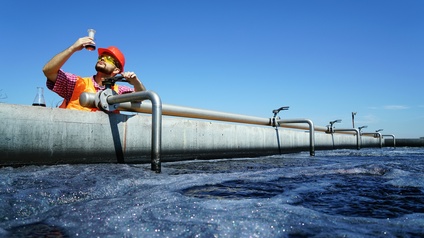 Person mit Helm steht an Wasseraufbereitungsanlage und blickt auf Testflasche mit Flüssigkeit