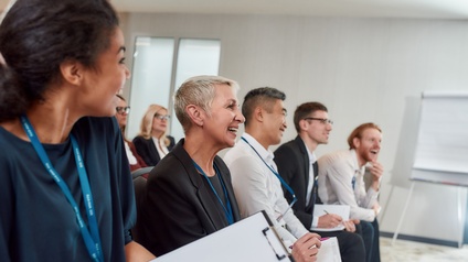 Personen im Publikum eines Konferenzraumes blicken freudig nach vorne