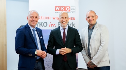 Drei lächelnde Männer stehen vor einem WKO-Rollup