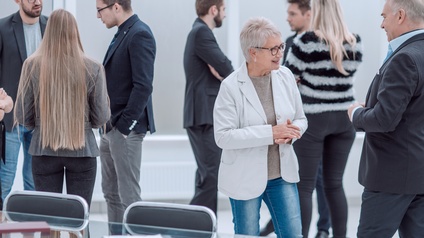 Personen in Businesskleidung stehen in einem hellen Raum neben einem Besprechungstisch und unterhalten sich