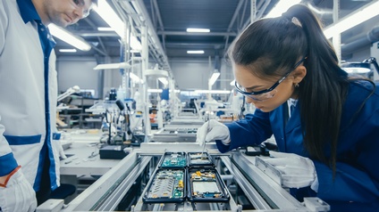 Aufnahme eines Lehrlings in einer Elektronikfabrik, der Leiterplatten von Hand zusammenbaut, während er am Fließband steht
