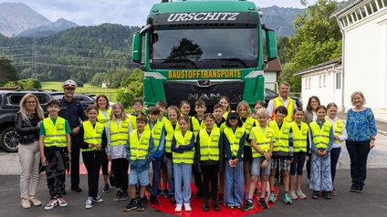 Eine Gruppe von Volksschülern mit ihrer Lehrerin und einem Polizisten vor einem LKW.