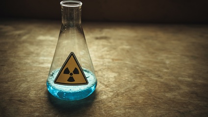 Laborglas mit blauer Flüssigkeit und Aufkleber Radioaktivitätszeichen: Gelbes schwarz umrandetes Dreieck, mittig gefüllter schwarzer Kreis umgeben von drei schwarzen abgerundeten Trapezen