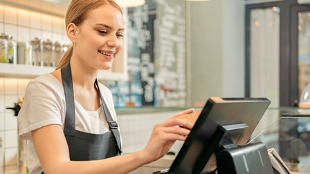 Person in Arbeitskleidung steht vor einer Kasse in einem Lebensmittelladen