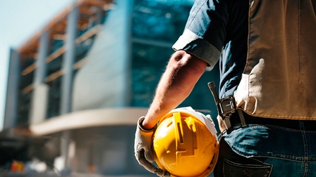 Ein Bauarbeiter mit Helm im Arm mit Blick auf Baustelle