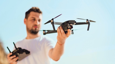 Ein Mann vor blauem Hintergrund hält eine Drohne in einer Hand