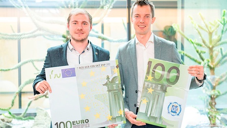 Christian Wipfler und Dominik Santner halten je einen Teil eines zerrissenen, großen 100-Euro-Geldscheins