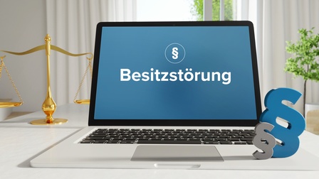 Aufgeklappter Laptop auf einem Tisch mit Schriftzug Besitzstörung und Icon Paragraph daneben stehen weitere Paragraphen auf der Tastatur und eine goldene Waagschale links dahinter