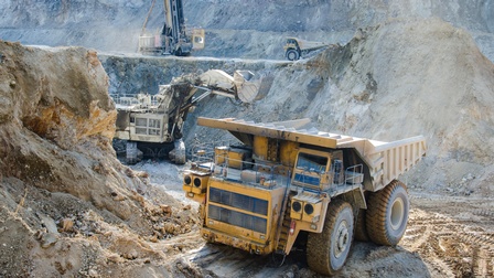 Großer gelber Bautransporter im Fokus in Baugrube stehend, im Hintergrund weitere Baumaschinen wie Bagger und Kräne