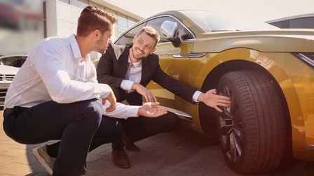 Zwei Personen neben gelbem Auto hockend auf Fahrzeugreifen deutend