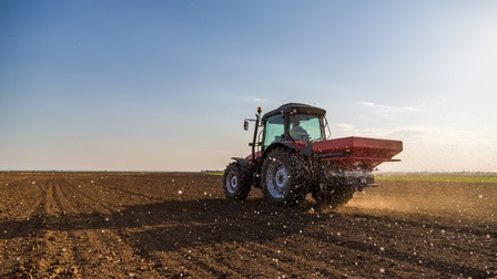 Ein Traktor in Rückansicht sprüht Flüssigkeit auf einen brauen Acker unter blauem Himmel