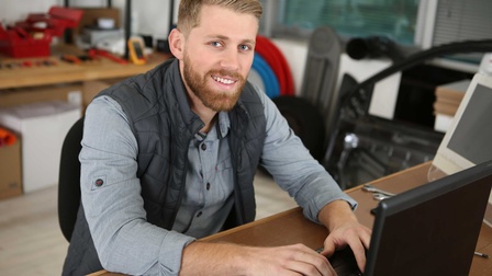 Ein Handwerker sitz in einer Werkstatt vor einem Laptop