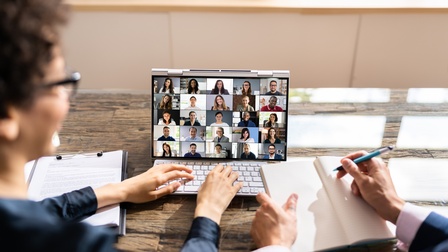 Personen blicken auf Laptopbildschirm mit mehreren online Teilnehmenden bei Meeting