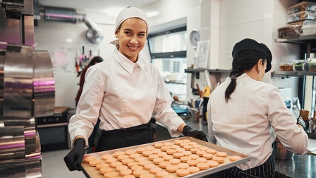 Eine junge Konditorin trägt ein Kuchenblech mit Gebäck