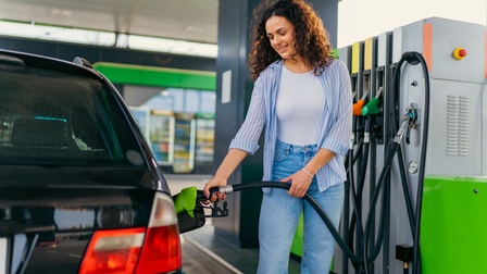 Lächelnde Person steht auf Tankstelle und hält Zapfhahn in Autotank