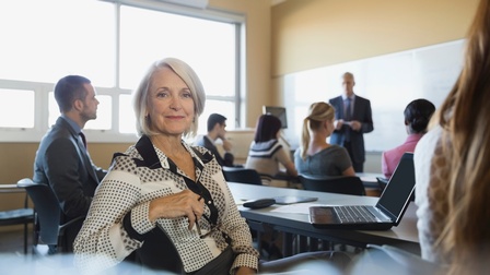 Im Fokus lächelnde Person in Seminarsituation mit anderen Menschen