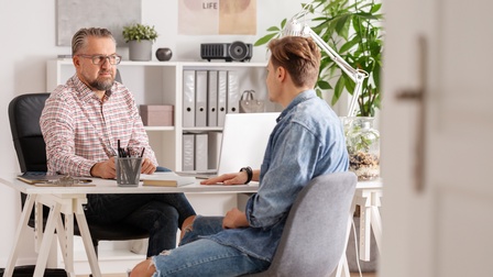 Personen sitzen an einem Schreibtisch und führen ein Gespräch in einem Büroraum