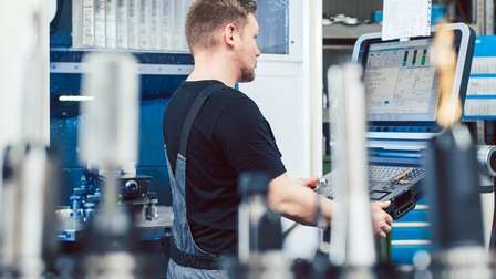 Person steht bei einer CNC Maschine in einer Werkstätte