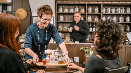 Lächelnde Person mit Brillen serviert weiteren Personen Tablet mit Tee
