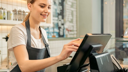 Person in Arbeitskleidung steht vor einer Kasse in einem Lebensmittelladen