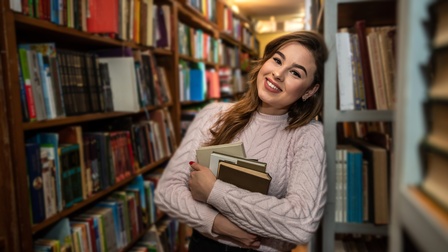 Person mit Büchern in der Hand steht in einer Bibliothek