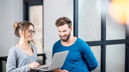 Zwei lächelnde Personen auf aufgeklapptes Notebook blickend