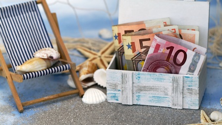 Geld in einer kleinen Schatztruhe neben Strandliege