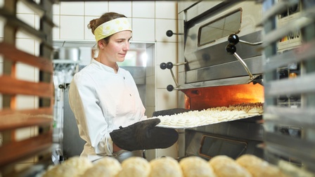 Eine junge Konditorin holt ein Blech frisches Baiser aus dem Ofen