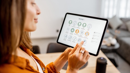 Eine Person kontrolliert auf einem Tablet die Einstellungen von Licht und Heizung für die Wohnung