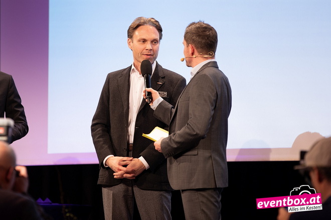 Zwei Männer auf Bühne, von denen einer den anderen interviewt